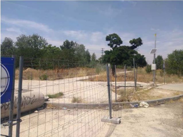 Foto terreno con valla metálica, suelo de tierra y árboles de fondo